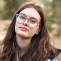 港彩极限校对编辑苏映雪的头像，年轻女性扎低马尾，米白色上衣，自然光下的浅灰背景，显得细致认真
